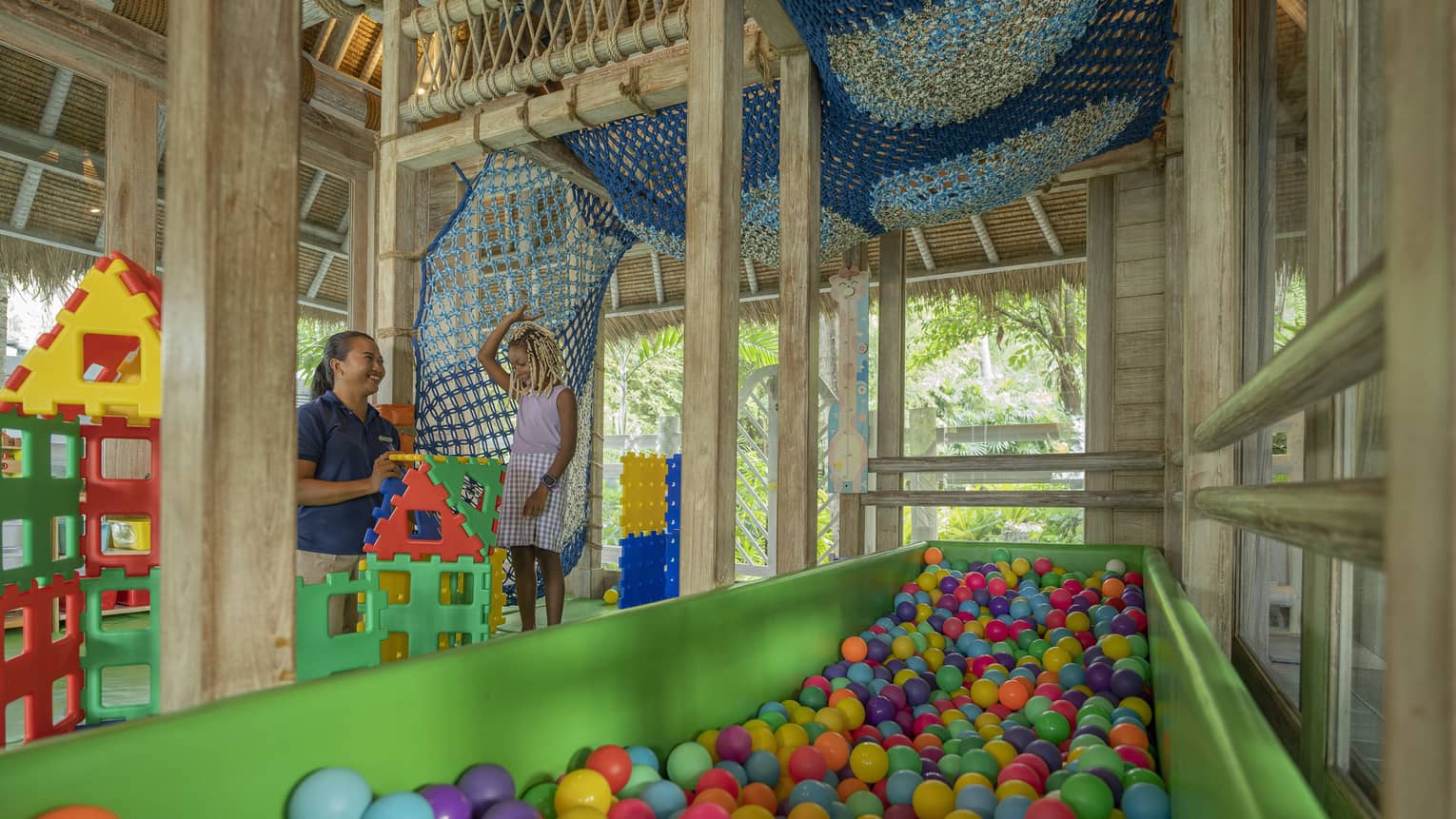 A smiling child building with large colourful blocks with a smiling care worker while in a large colourful indoor playground.
