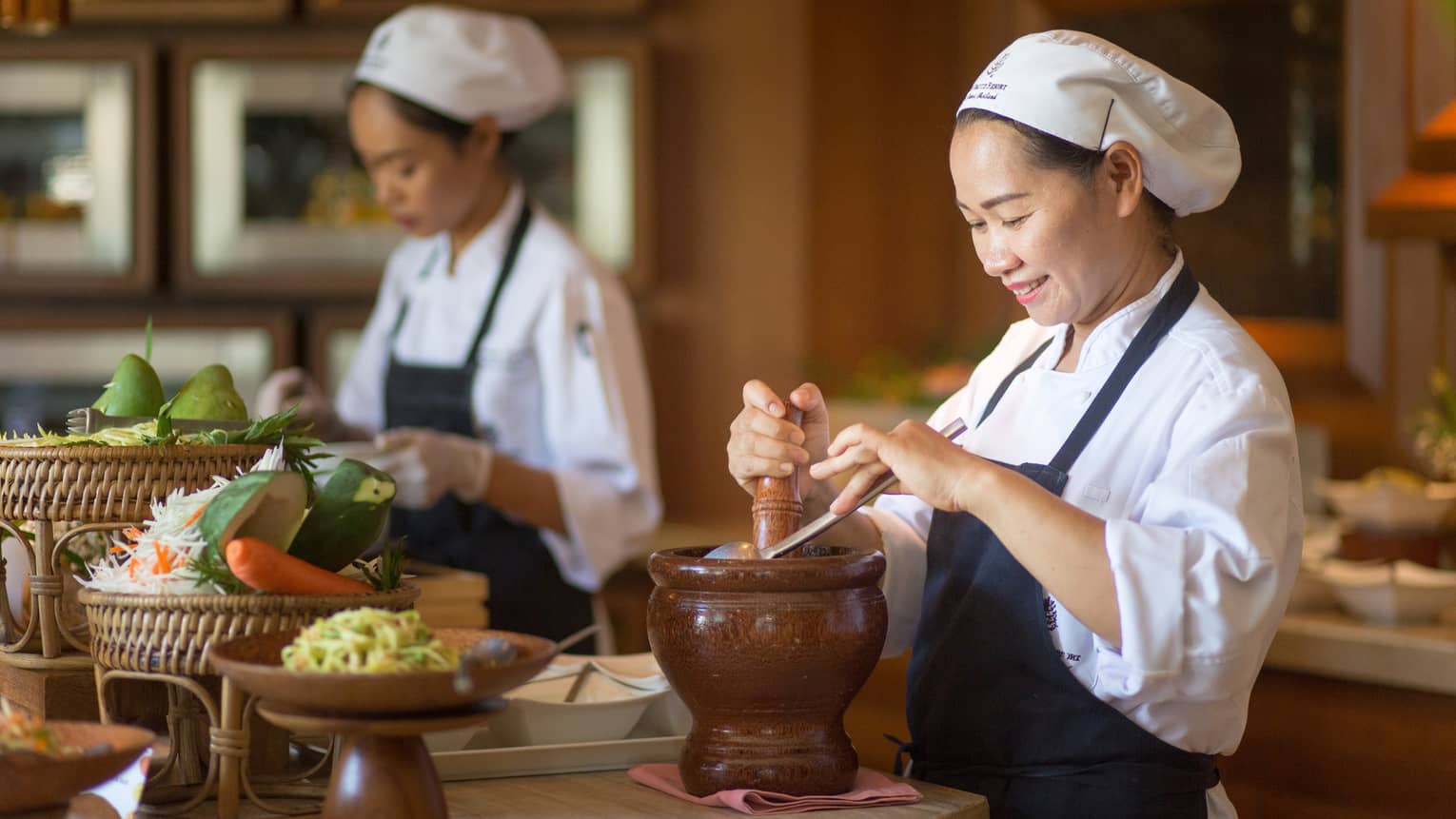 Two chefs in uniform prepare authentic Thai cuisine dishes at counter with fresh vegetables