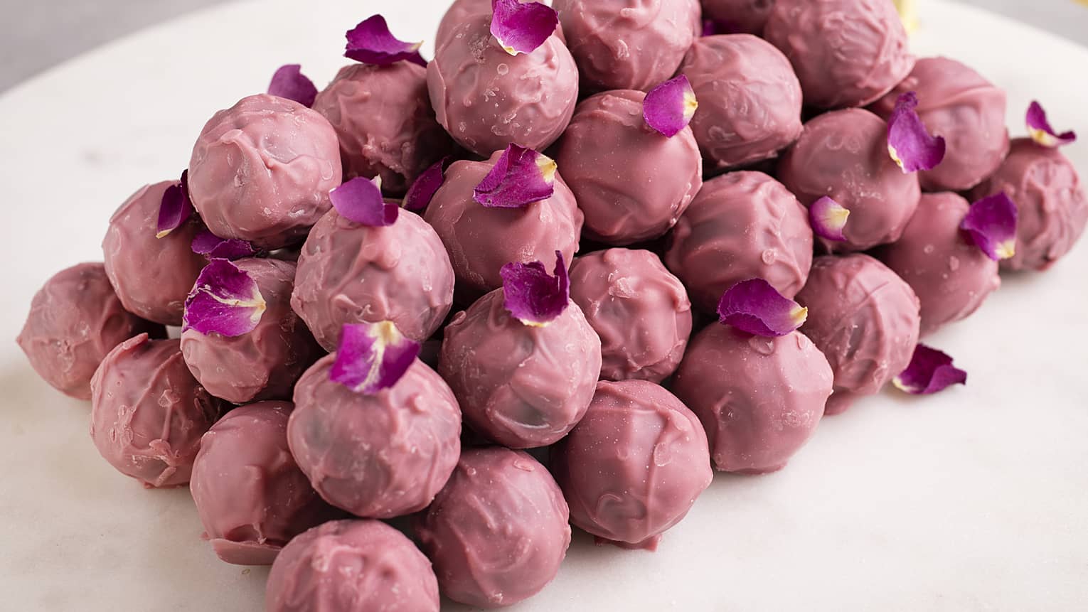 A stack of rose-colored chocolate pralines sprinkled with purple flower petals