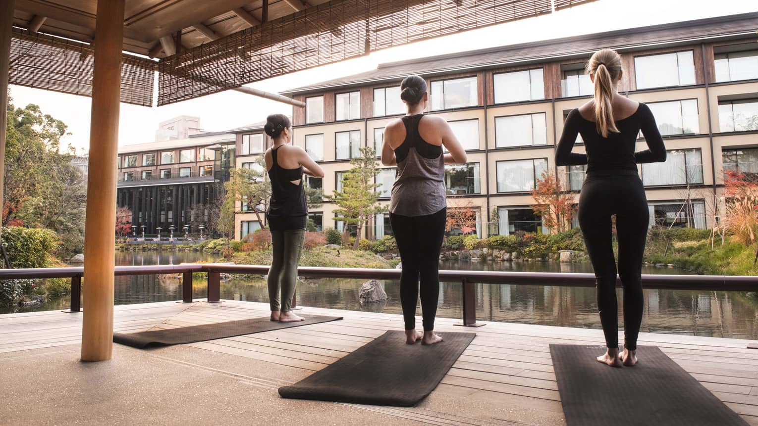 Back of three women wearing fitness clothes standing in yoga pose, facing buildings
