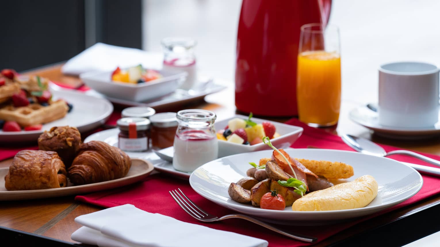 Breakfast foods (waffles, pastries, omelette with potatoes, fruit, etc.), orange juice and coffee on a table
