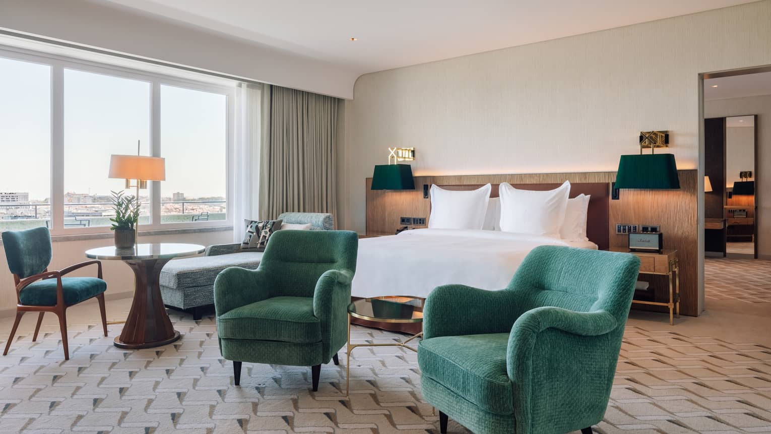 Hotel room with white king bed, two green armchairs, table and chaise