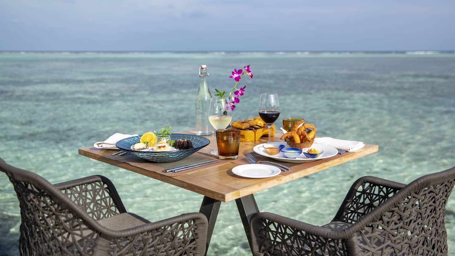 Outdoor patio table with seafood entrees, glasses of wine overlooking blue lagoon