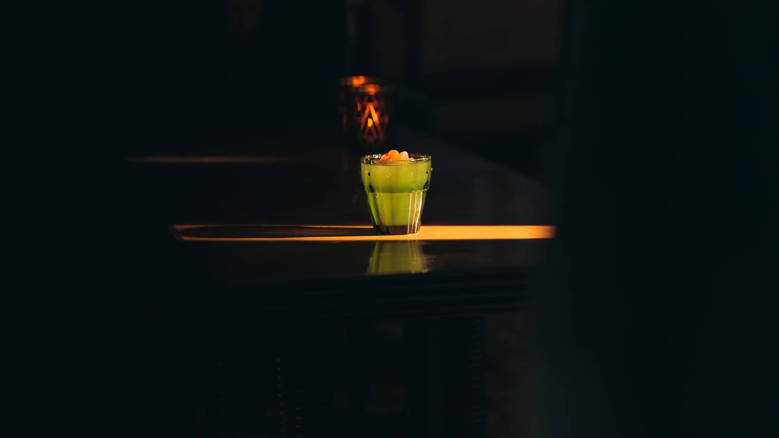 Light shining on glass of green juice with orange fruit on top.