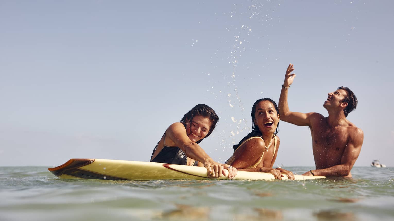 Two women and a man holding onto a surfboard in the ocean.