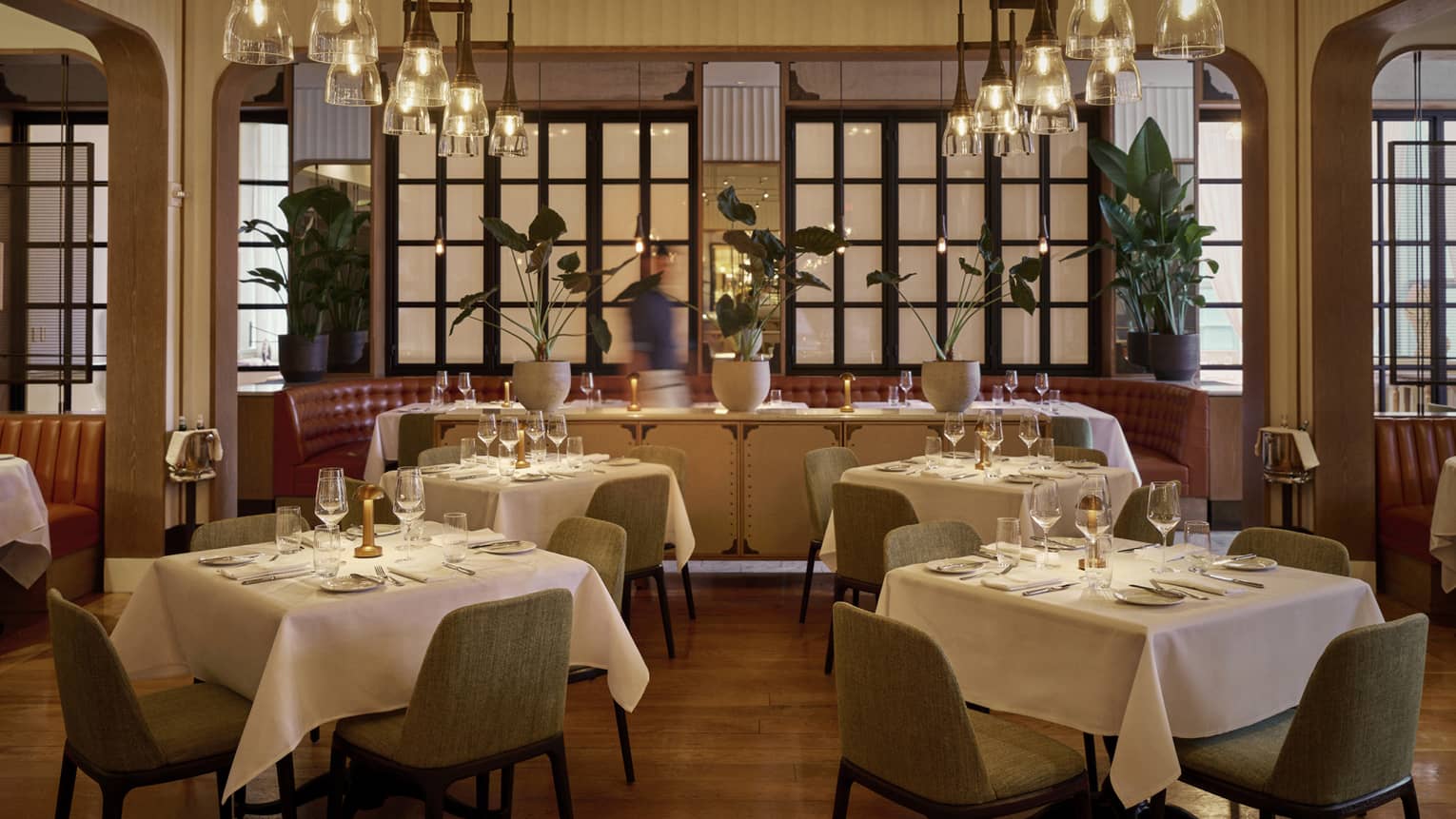 Dining room with dining tables set with tablecloths and glasses, and lights from the ceiling