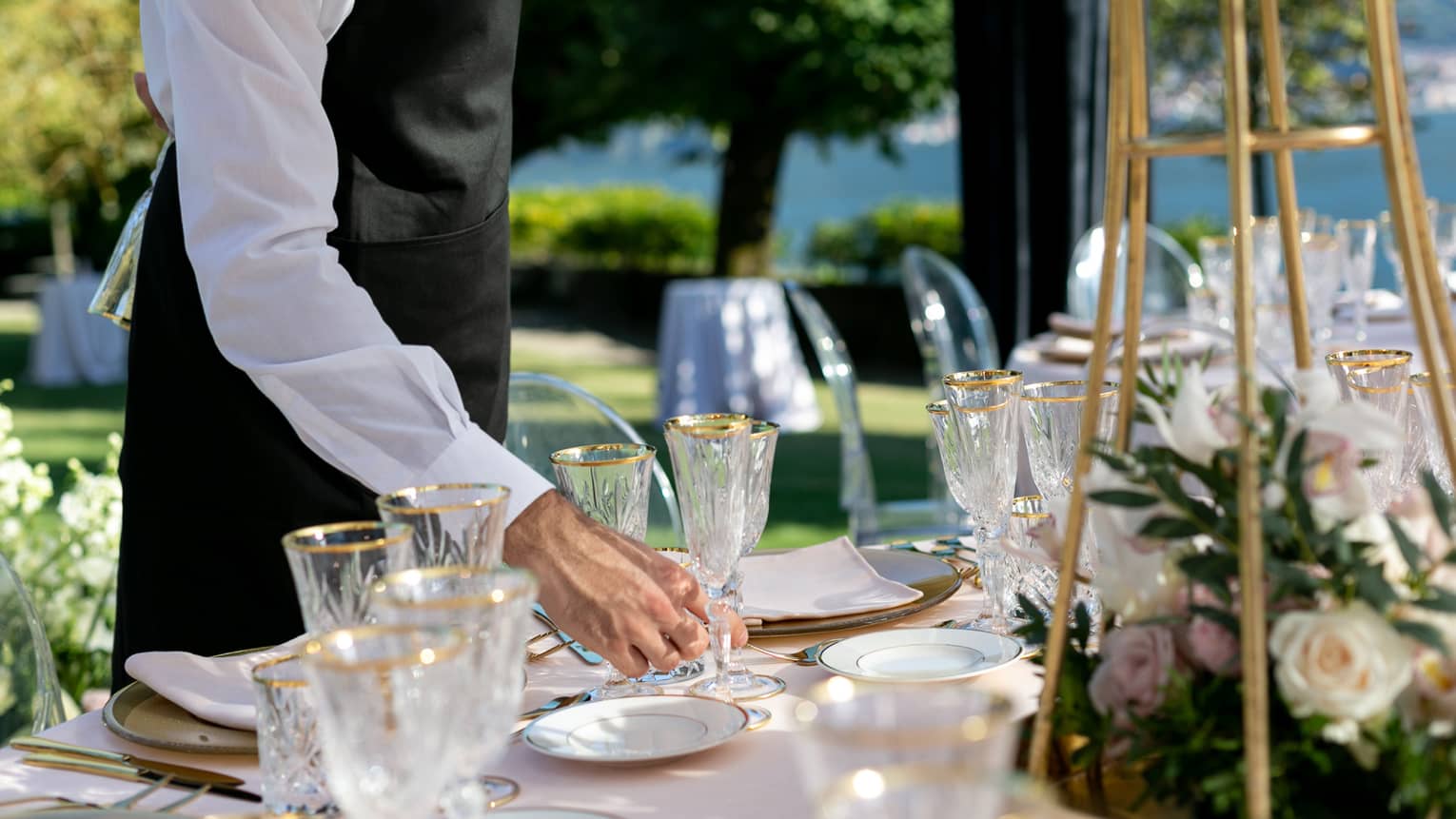 Wedding reception, hotel staff places gold rimmed wine glass on outdoor dining table