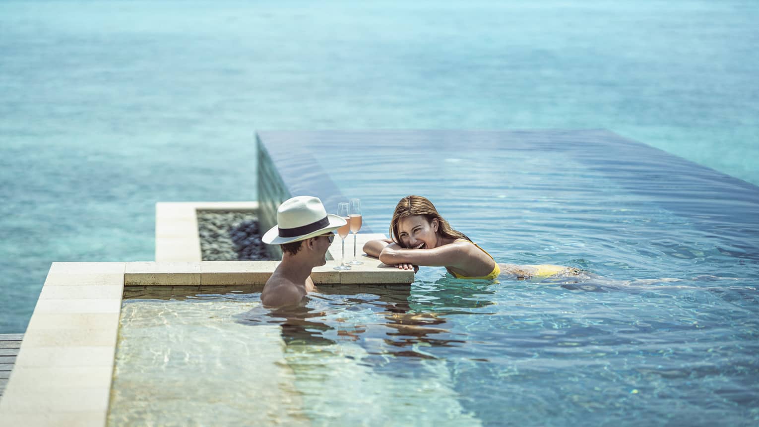 Couple relaxes with two glasses of wine in the infinity-edge pool