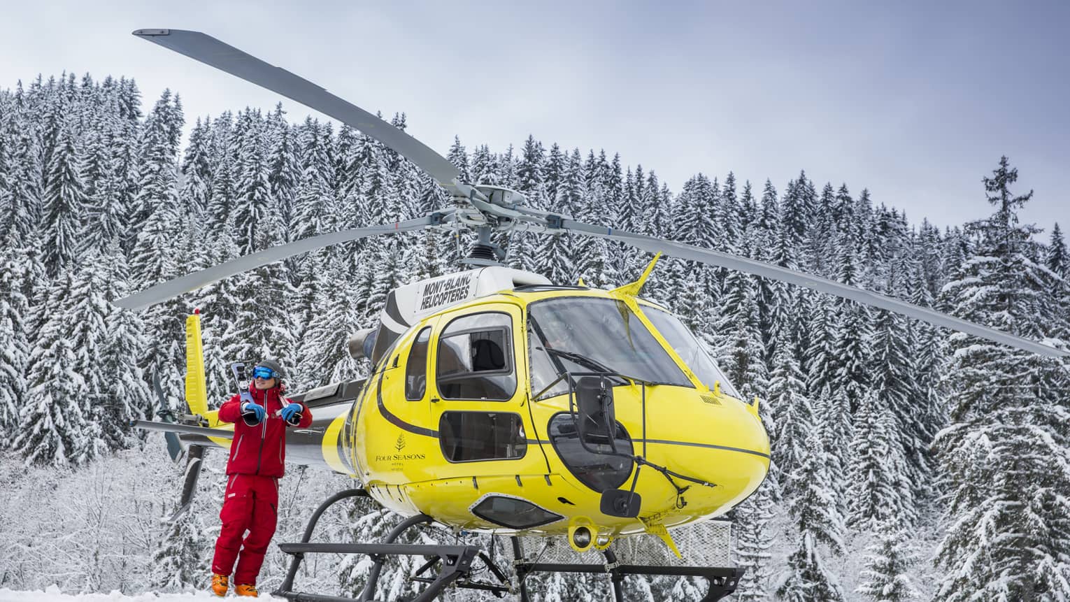 A yellow helicopter rests atop a snow covered mountain in Megeve
