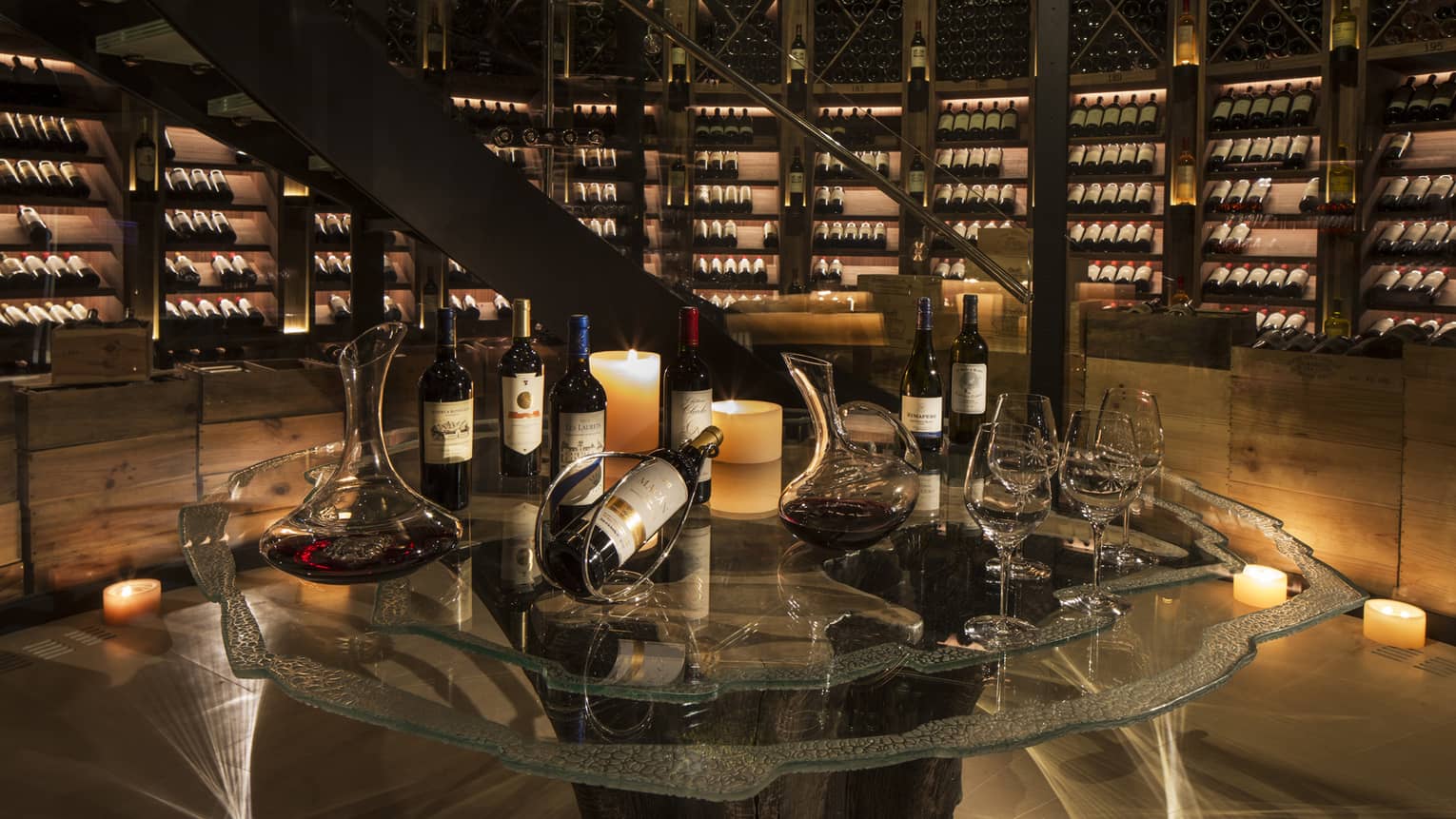 Bottles of wine are arranged for a tasting within an expansive, candlelit wine cellar