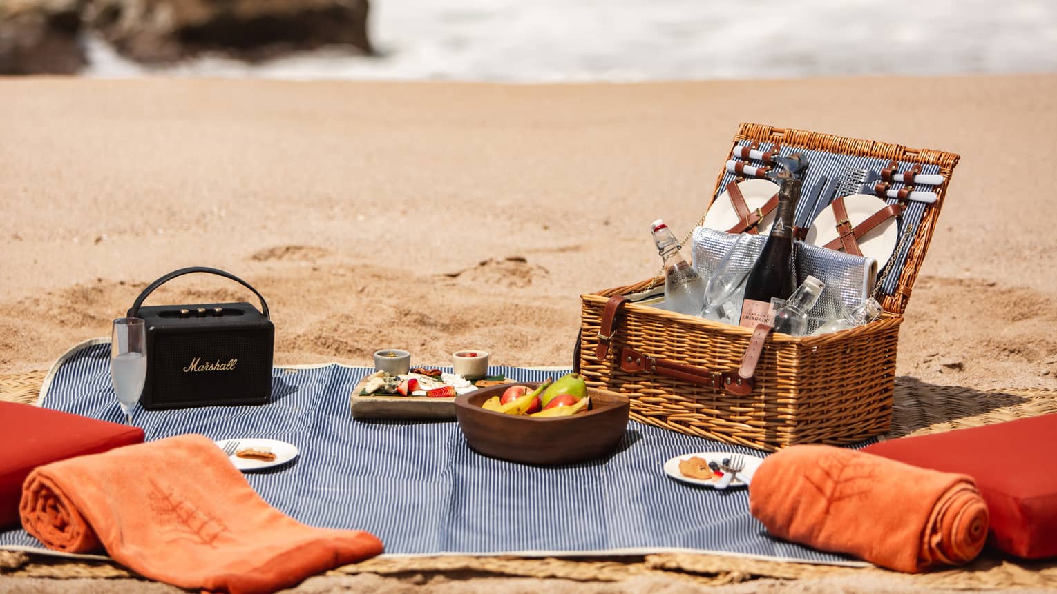 Picnic set on the beach, complete with basket, food, two towels and a Marhsall Bluetooth speaker