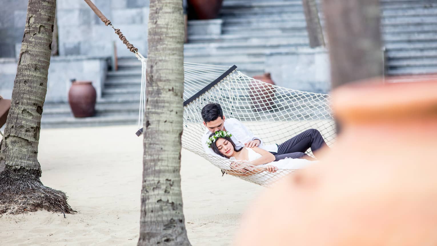 Bride and groom lounge in hammock on sand beach