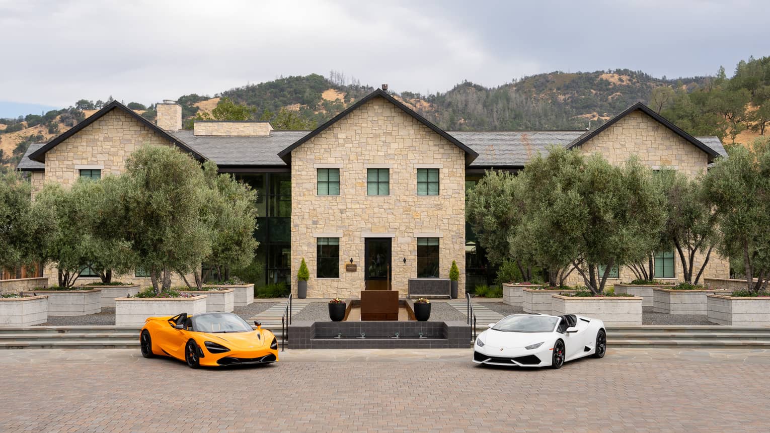 A white sports car and an orange sports car are parked in front a stately stone building