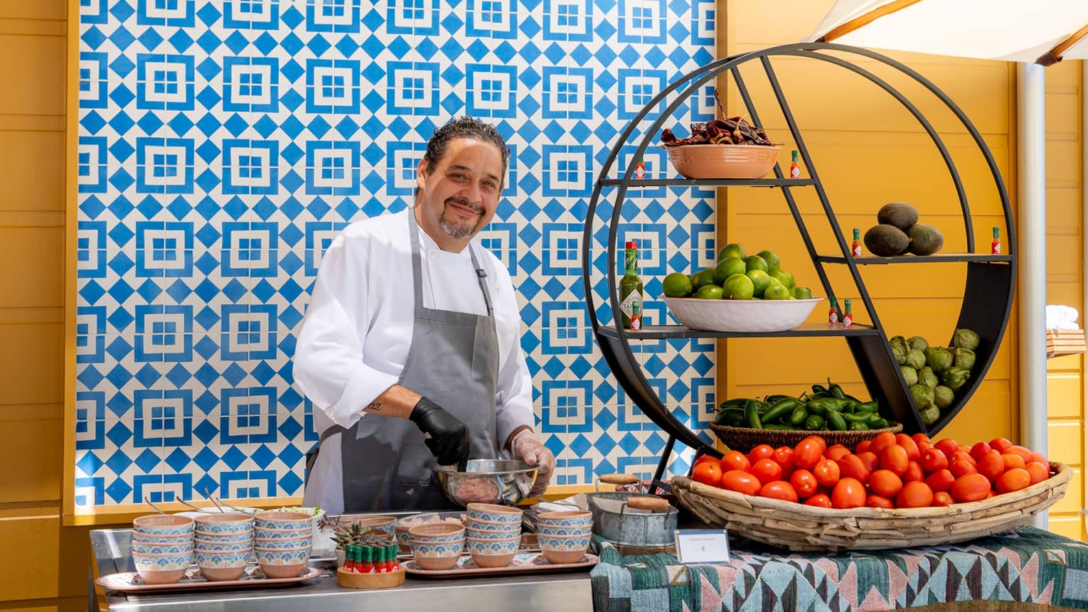 A chef wearing an apron and standing next to a display of fruits and vegetables