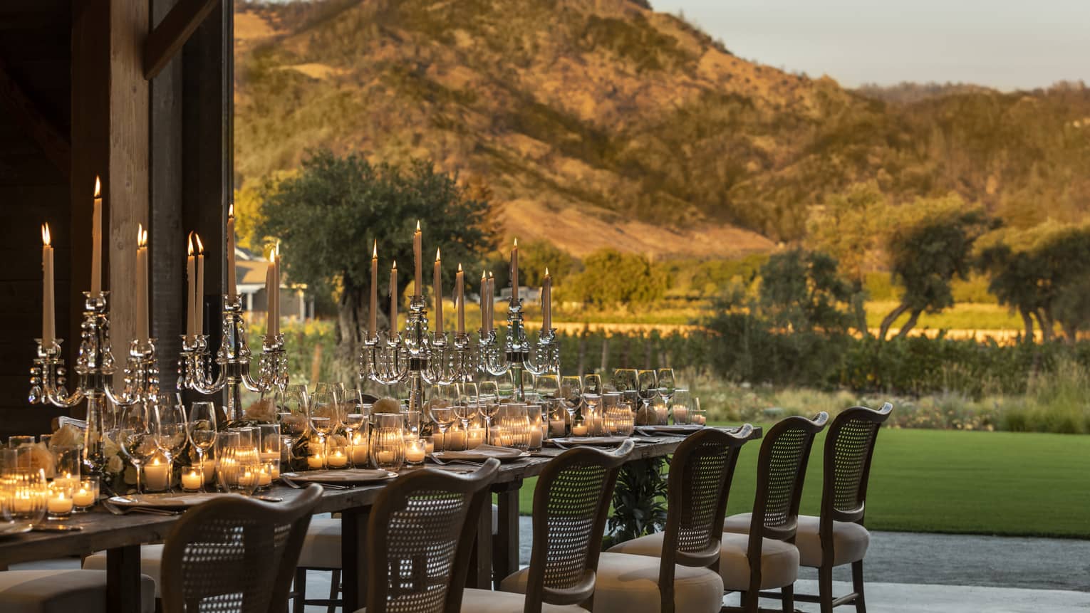 A long table with candles outside near mountains.