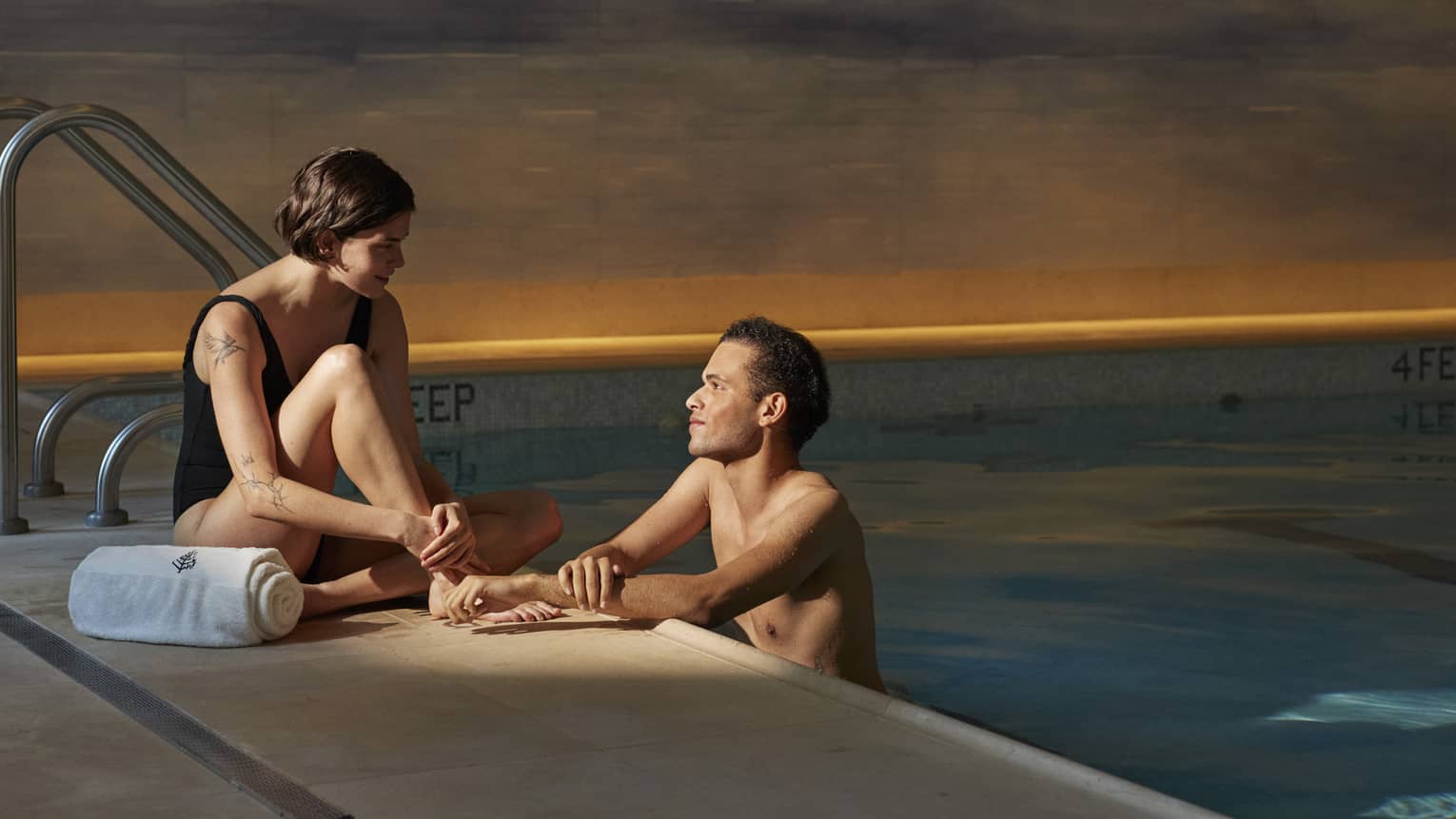 Person sitting poolside with a towel talking to another person leaning on the edge of the pool at Four Seasons luxury hotel