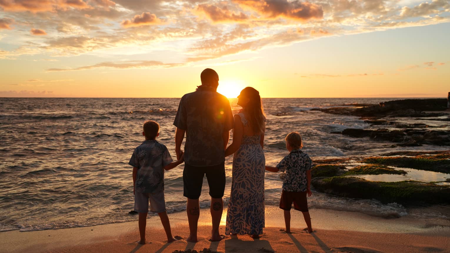 A family of four poses on a beach at sunset, facing away from the camera