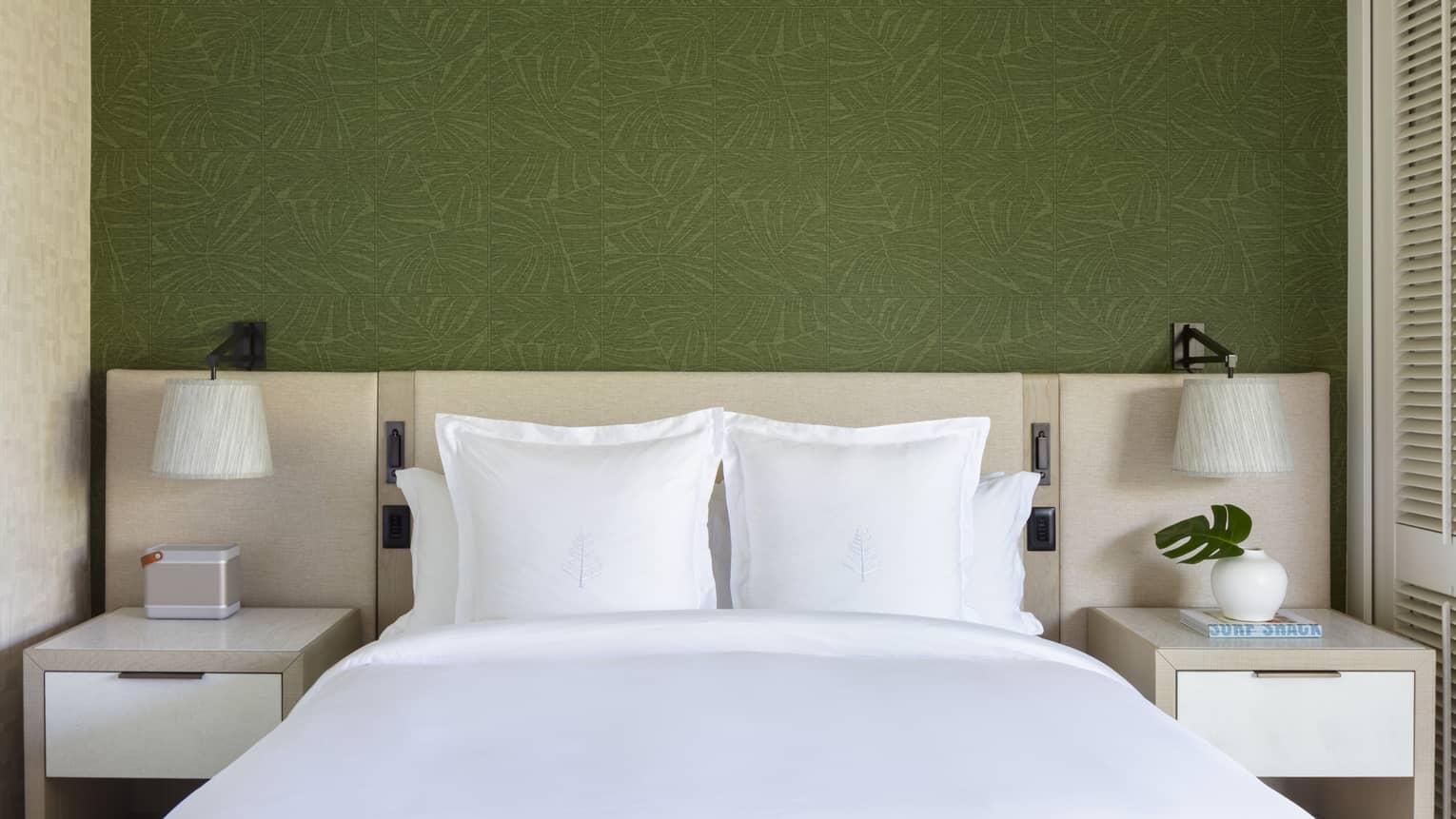 King bed with white sheets and Four Seasons logo on the pillows, set against green wallpaper