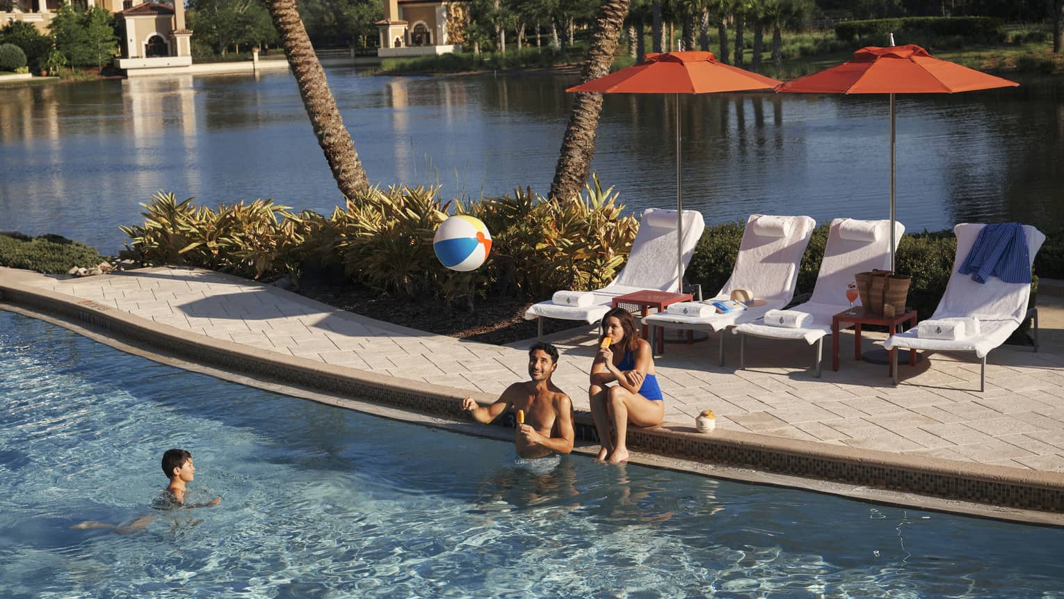 Two adults play with kid and a beach bar in the family pool at luxury resort