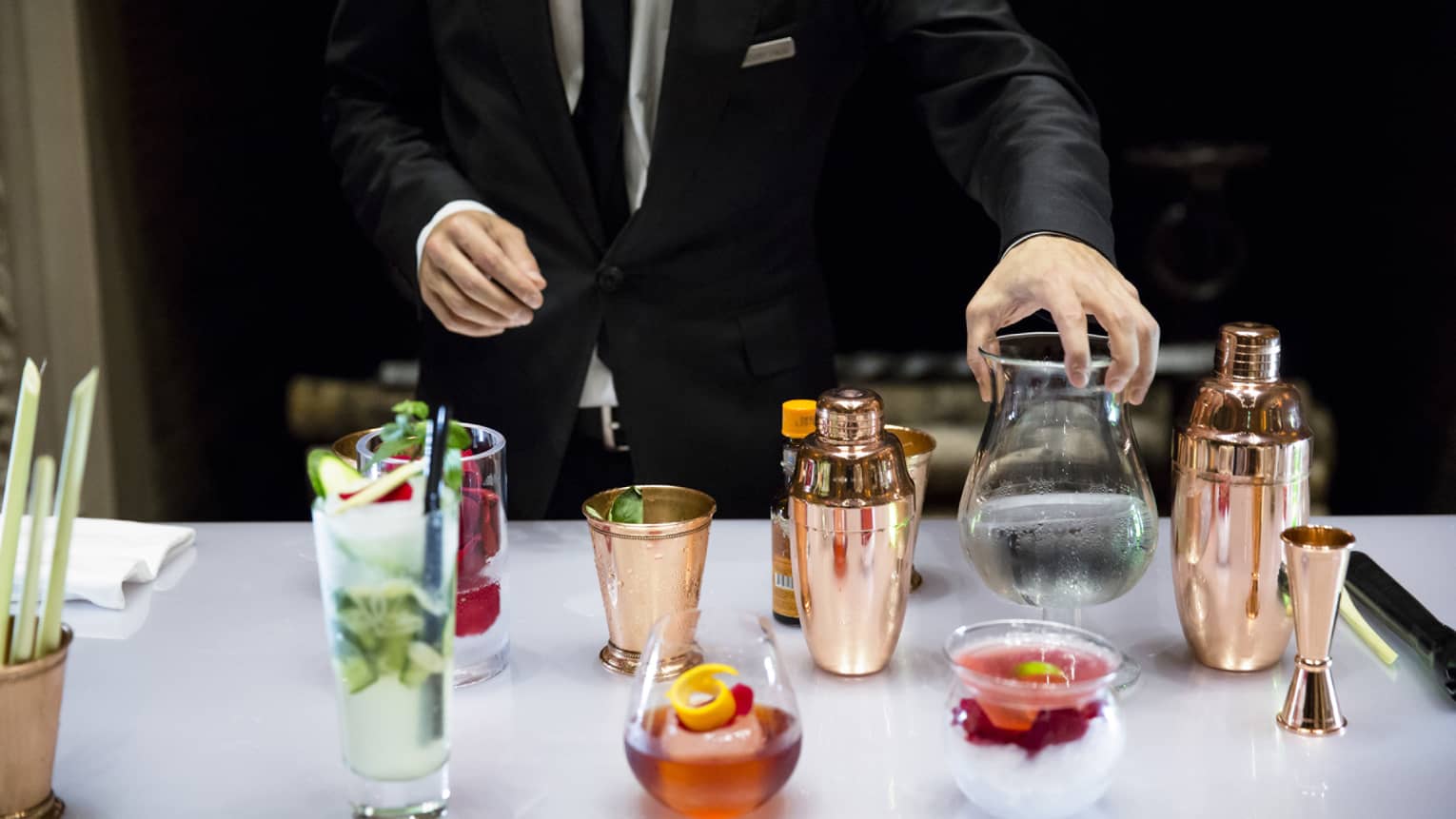 Bartender holds cocktail glass on bar beside copper shakers, fruity cocktails
