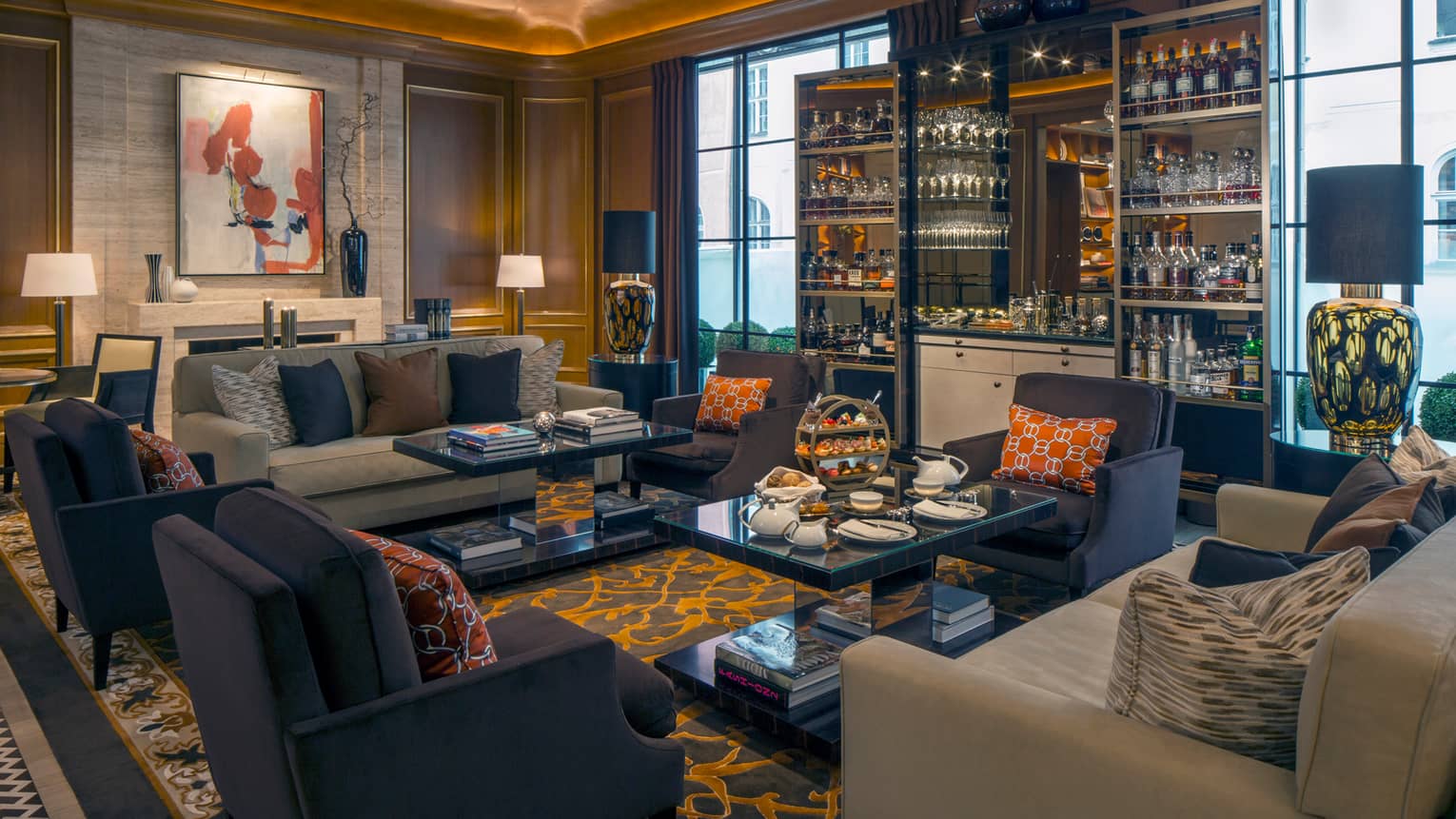 Dark blue armchairs, light sofas around dark glass coffee tables in front of display cabinet with wine, liquor, glasses