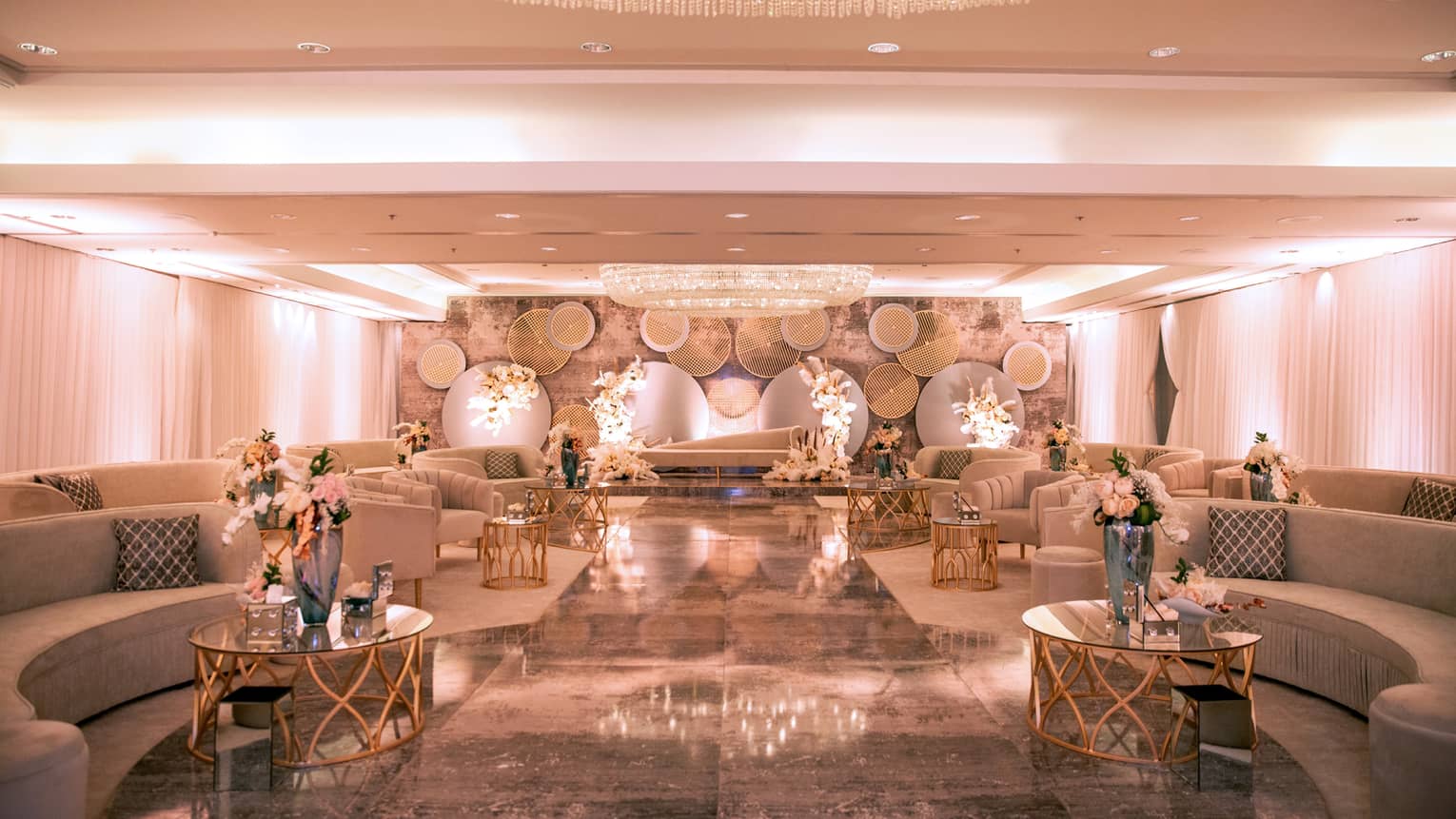 Elegant ballroom with rows of curved sofas, coffee tables and flowers under large dome chandelier