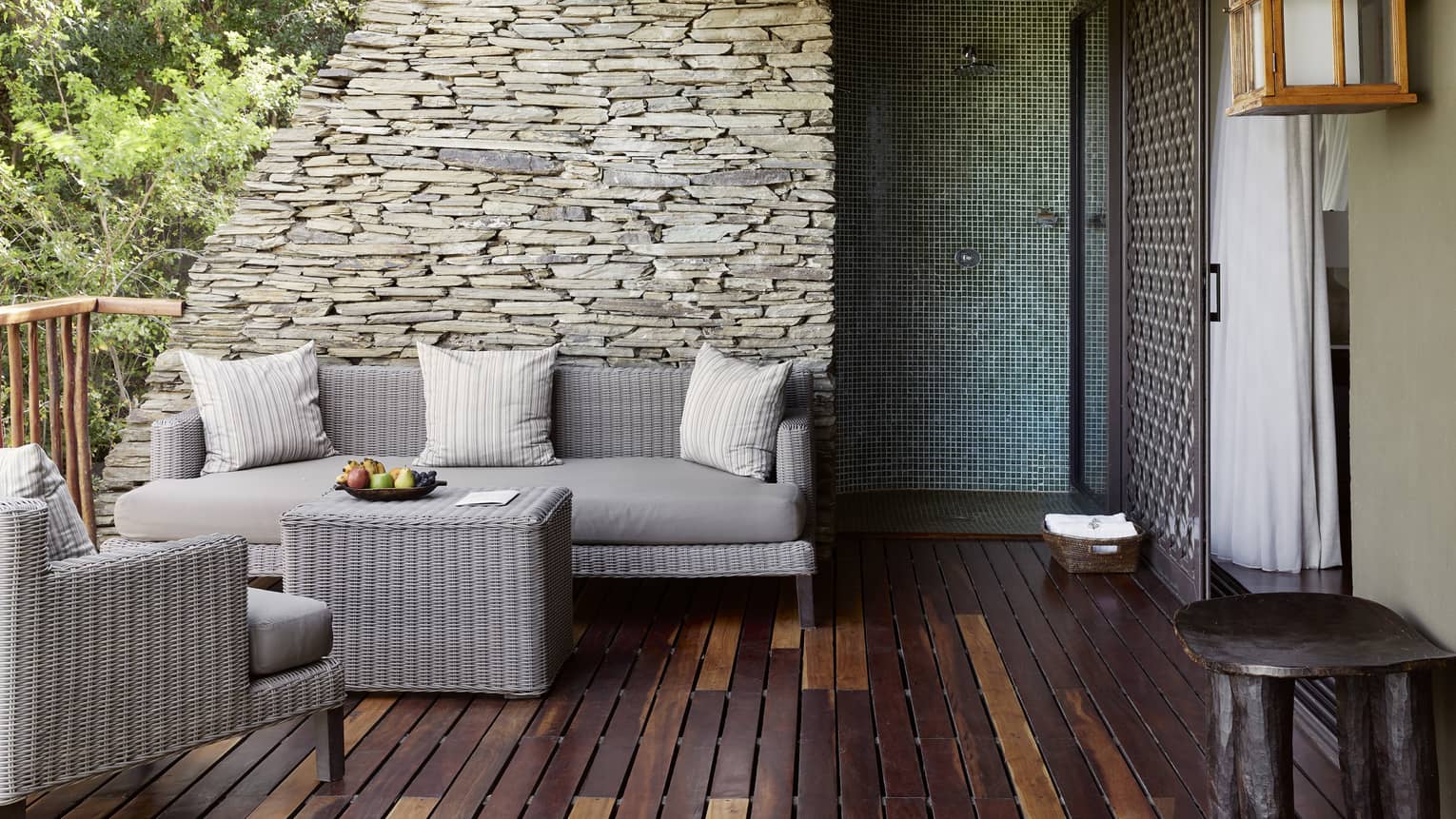 Wood-slatted terrace with neutral wicker seating vignette against stacked stone wall and sliding door to right