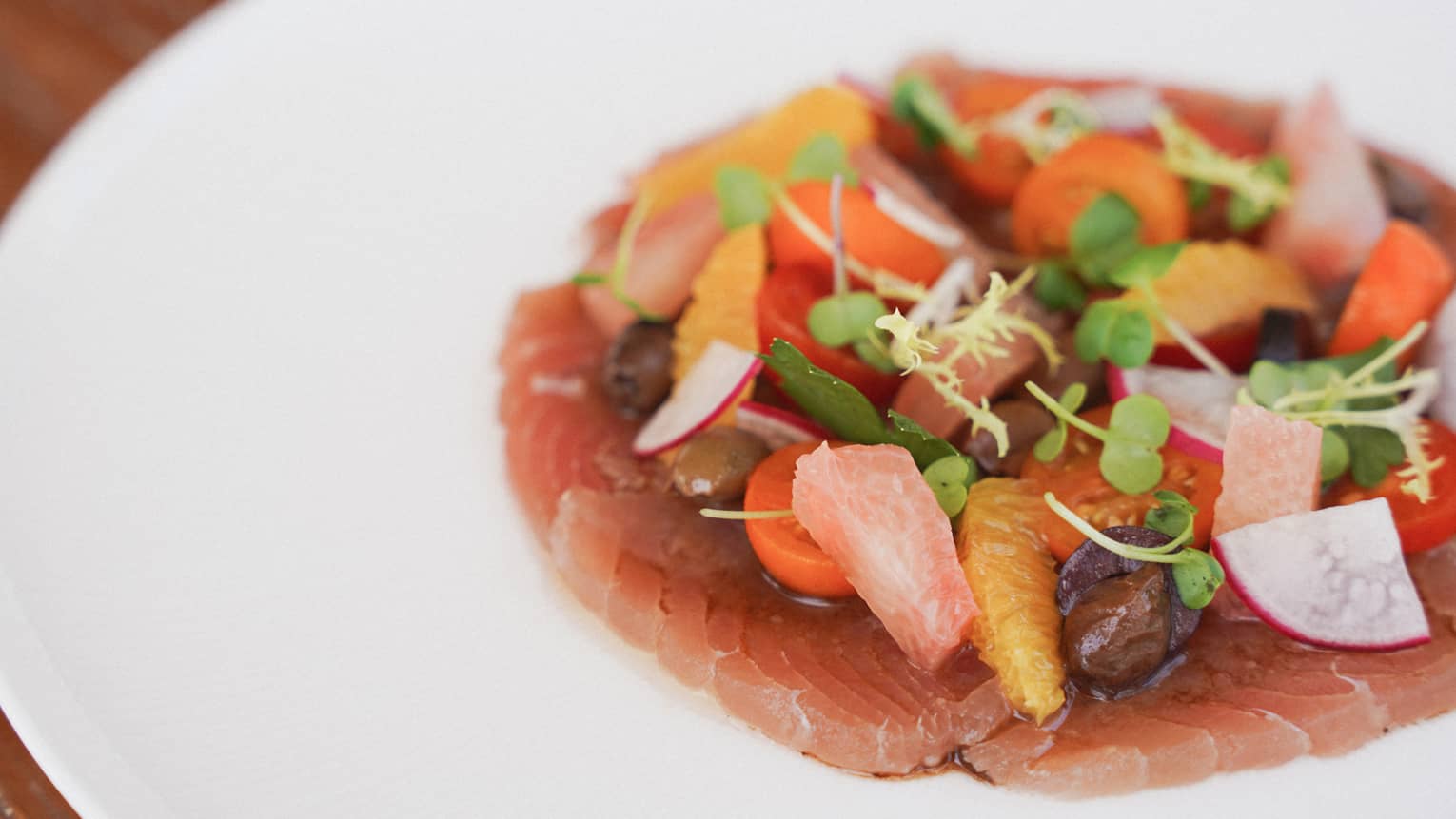 A white plate holds slices of reddish-pink fish topped with colorful garnishes.