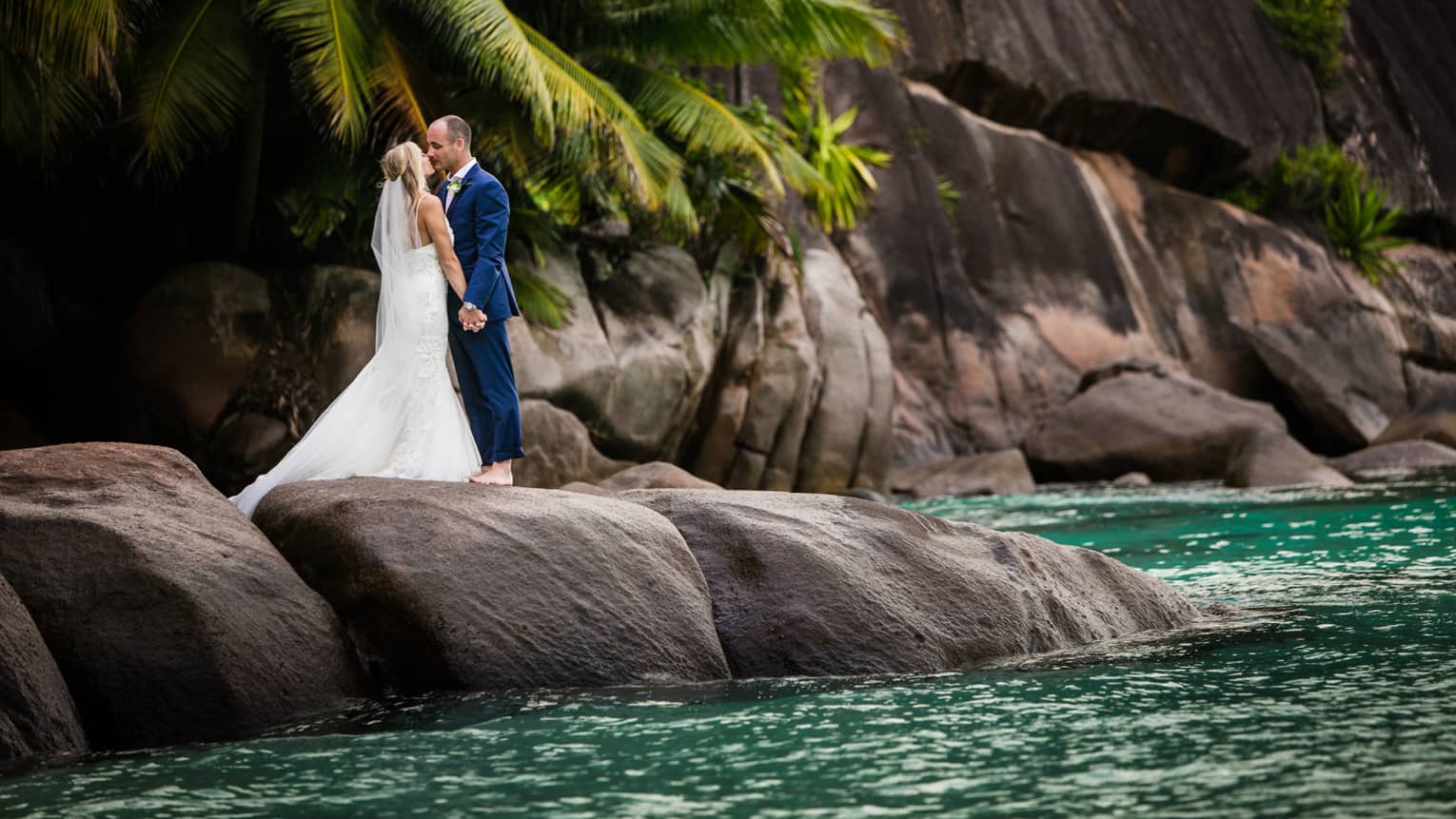 Bride and groom pose on rocks on ocean shore