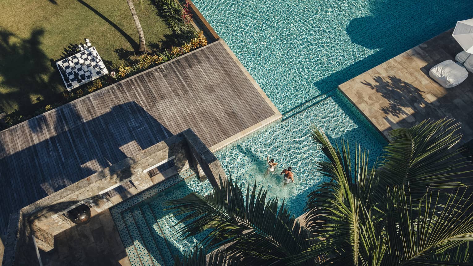 Aerial view of sparkling blue pool surrounded by decking and palm trees