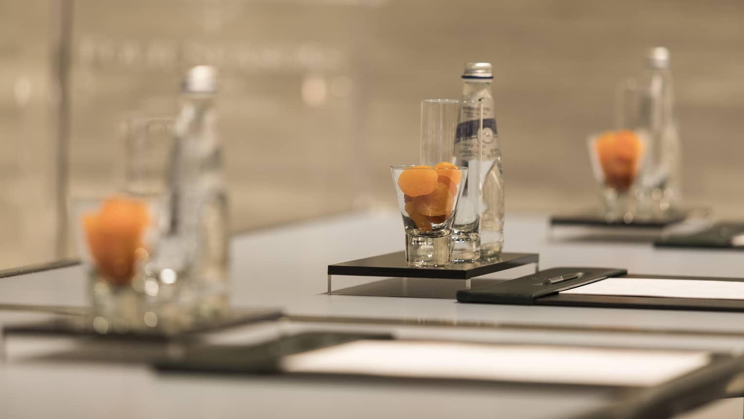 Close-up of meeting table place setting with agenda, dried apricots in glass, bottle of sparkling water