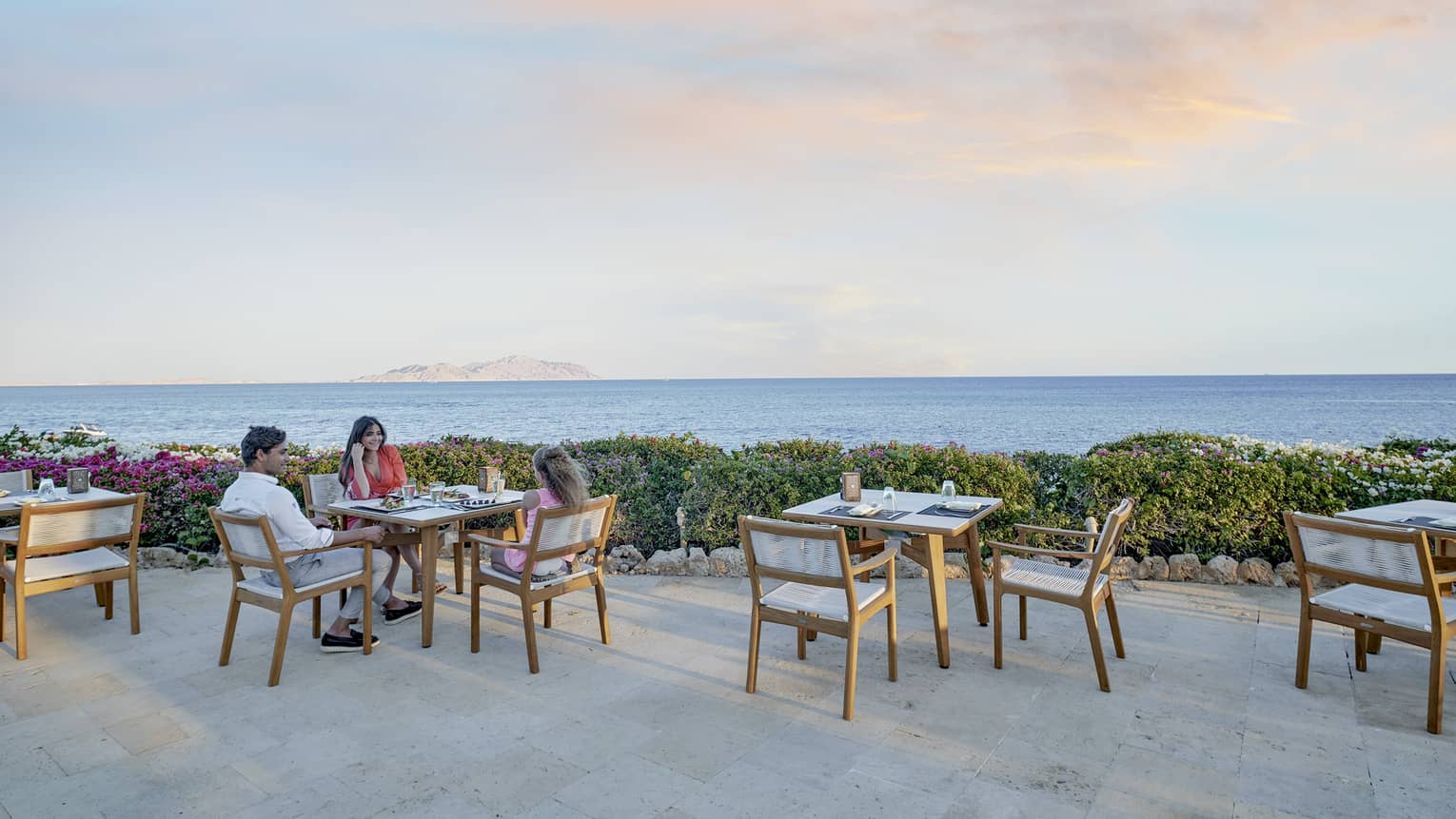 Man and woman sit at dining table on outdoor restaurant terrace, sea view