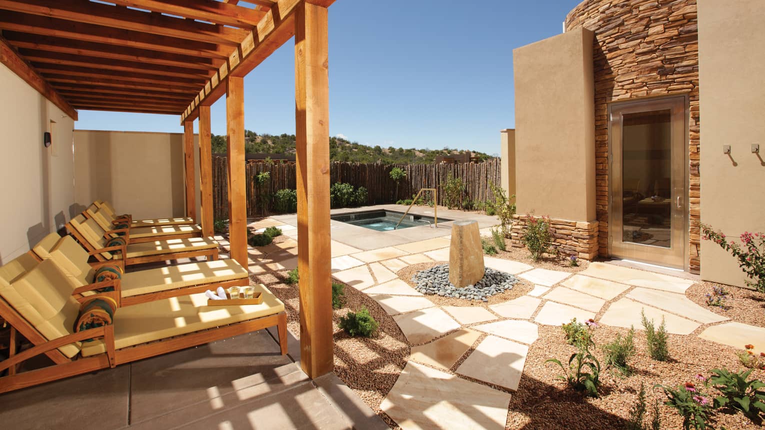 Shaded lounge chairs overlooking a stone patio spa area with a jacuzzi