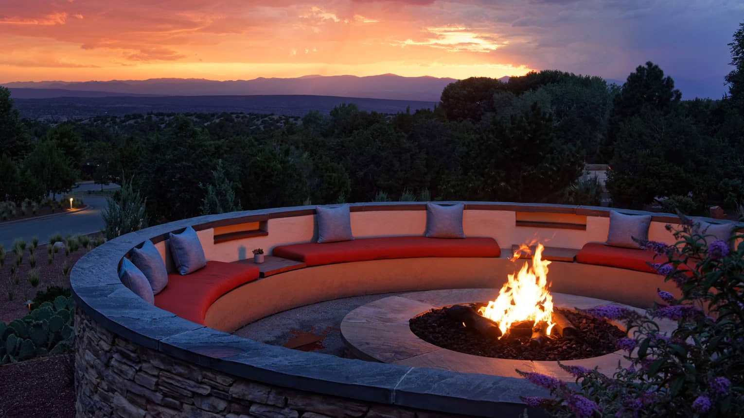 Fire pit with seating surrounding it and a sunset in the background.