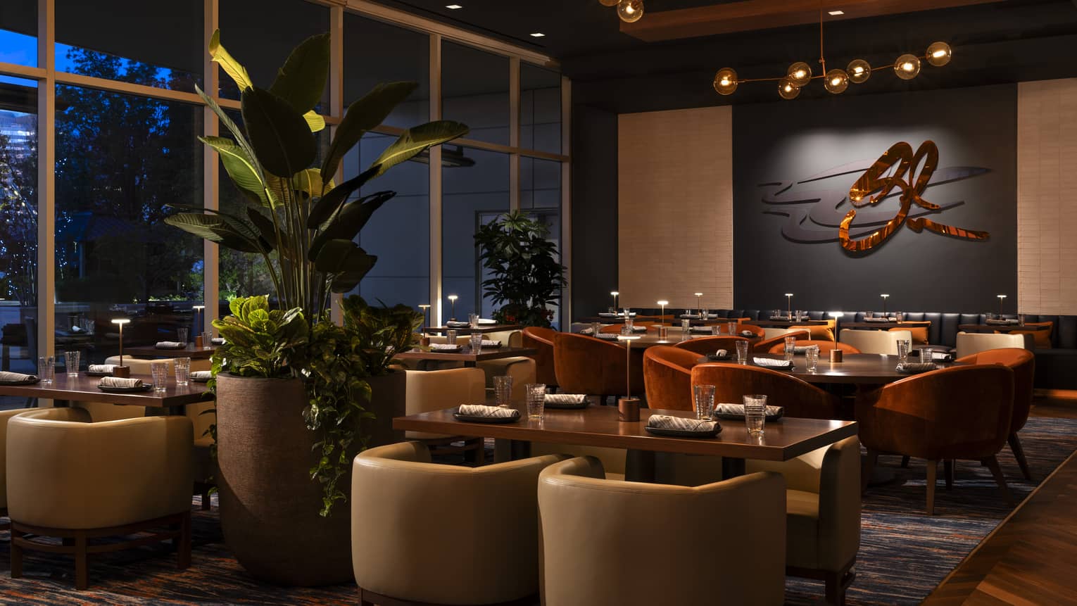 Elegant restaurant in a luxury hotel, featuring modern décor, warm lighting, plush seating and large windows with plants adding to the ambiance