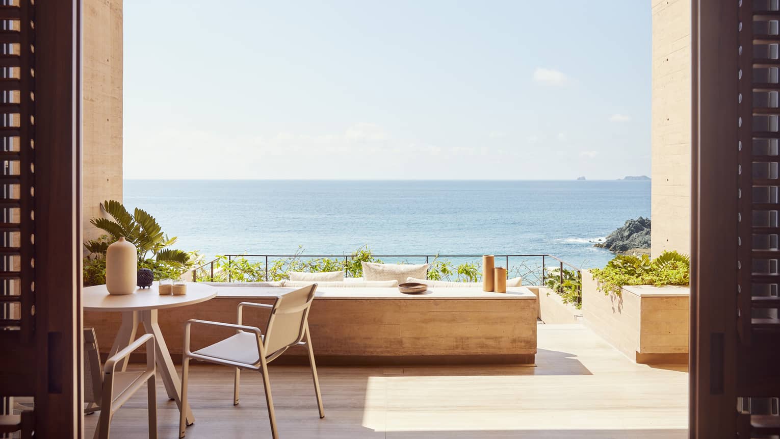 The exterior of a beachfront room with a small table and a large opening looking out at an ocean.