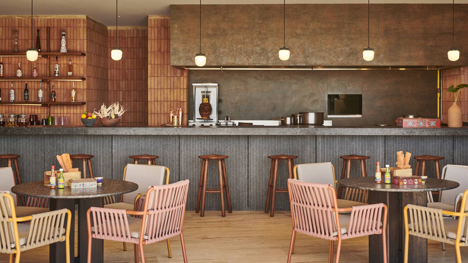 A room with round table and brightly coloured chairs near a counter with stools.