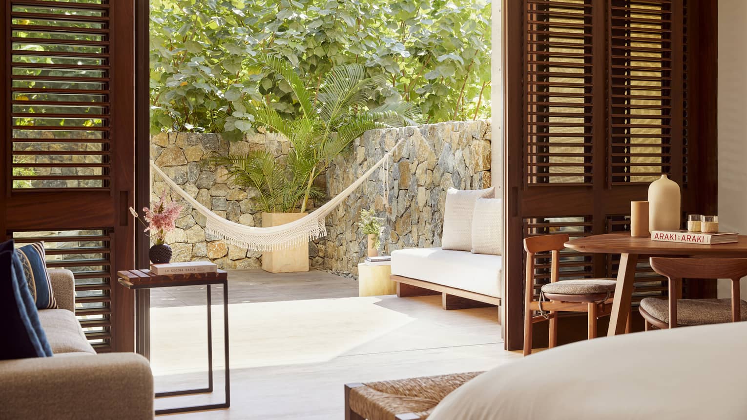A room with a bed, sofa, small table and open doors leading outside.