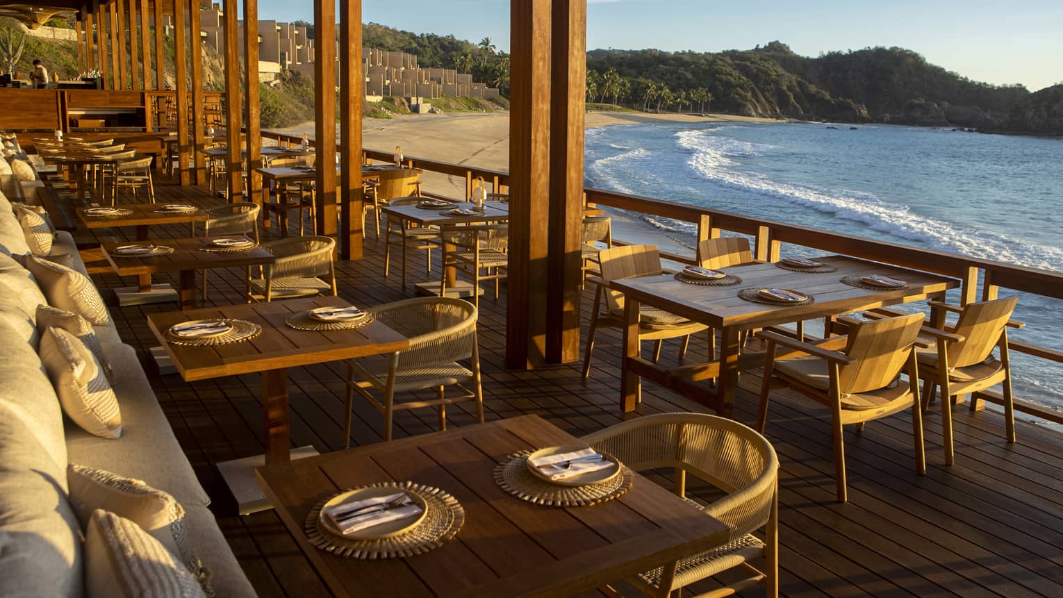 A sunlit restaurant with wood tables and chairs overlooking the ocean.