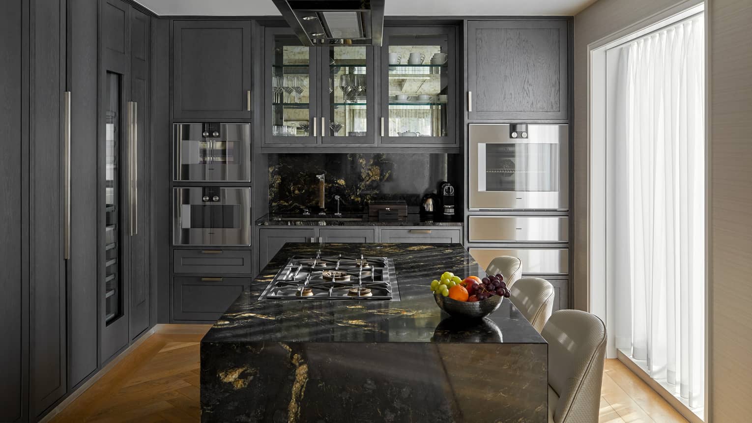 A kitchen area with dark walls and island, large window and stools.