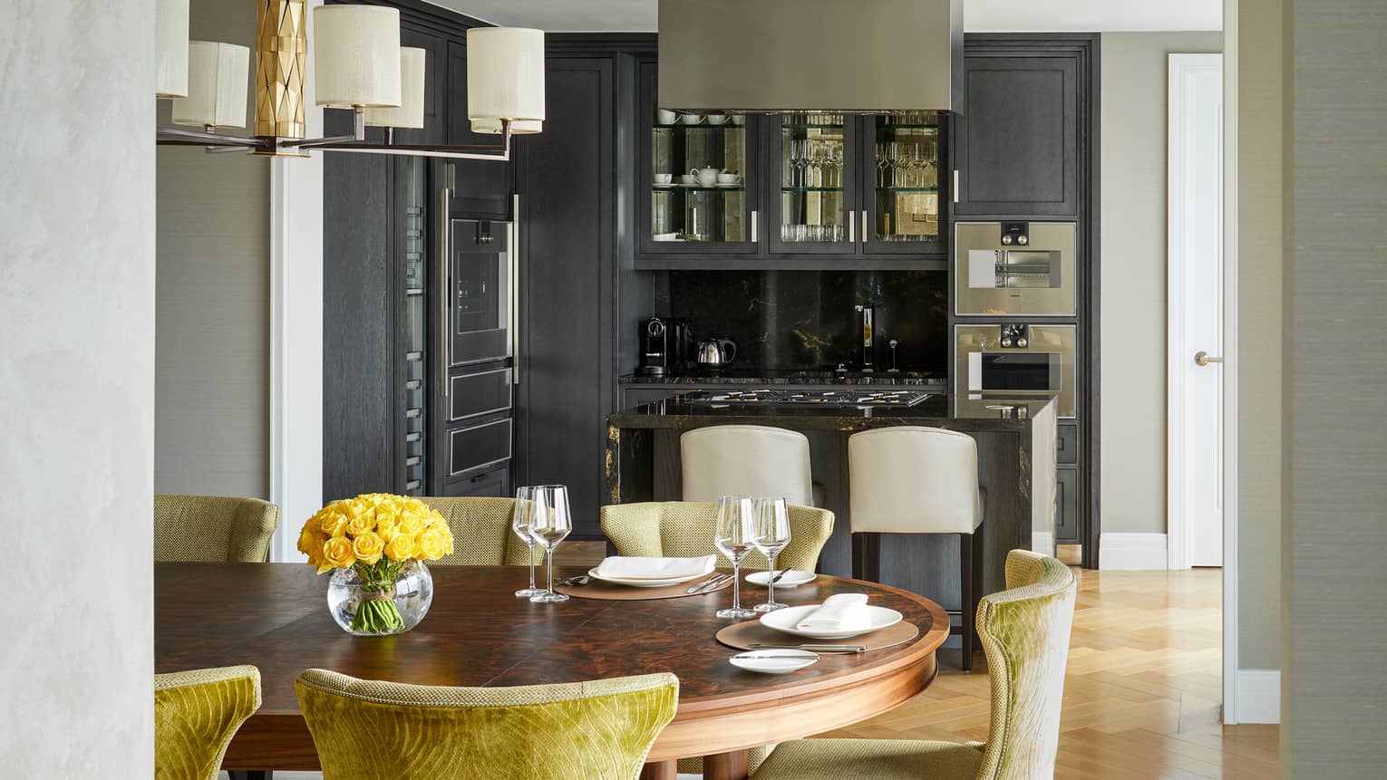 A dining and kitchen area with large wood table, counter with stools and cabinets with glass doors.