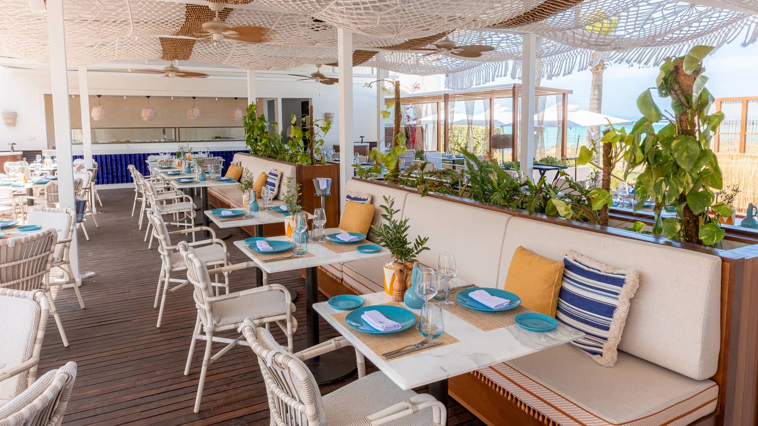 Open-air BLU beachfront restaurant with white banquette seating and white chairs under netted ceiling