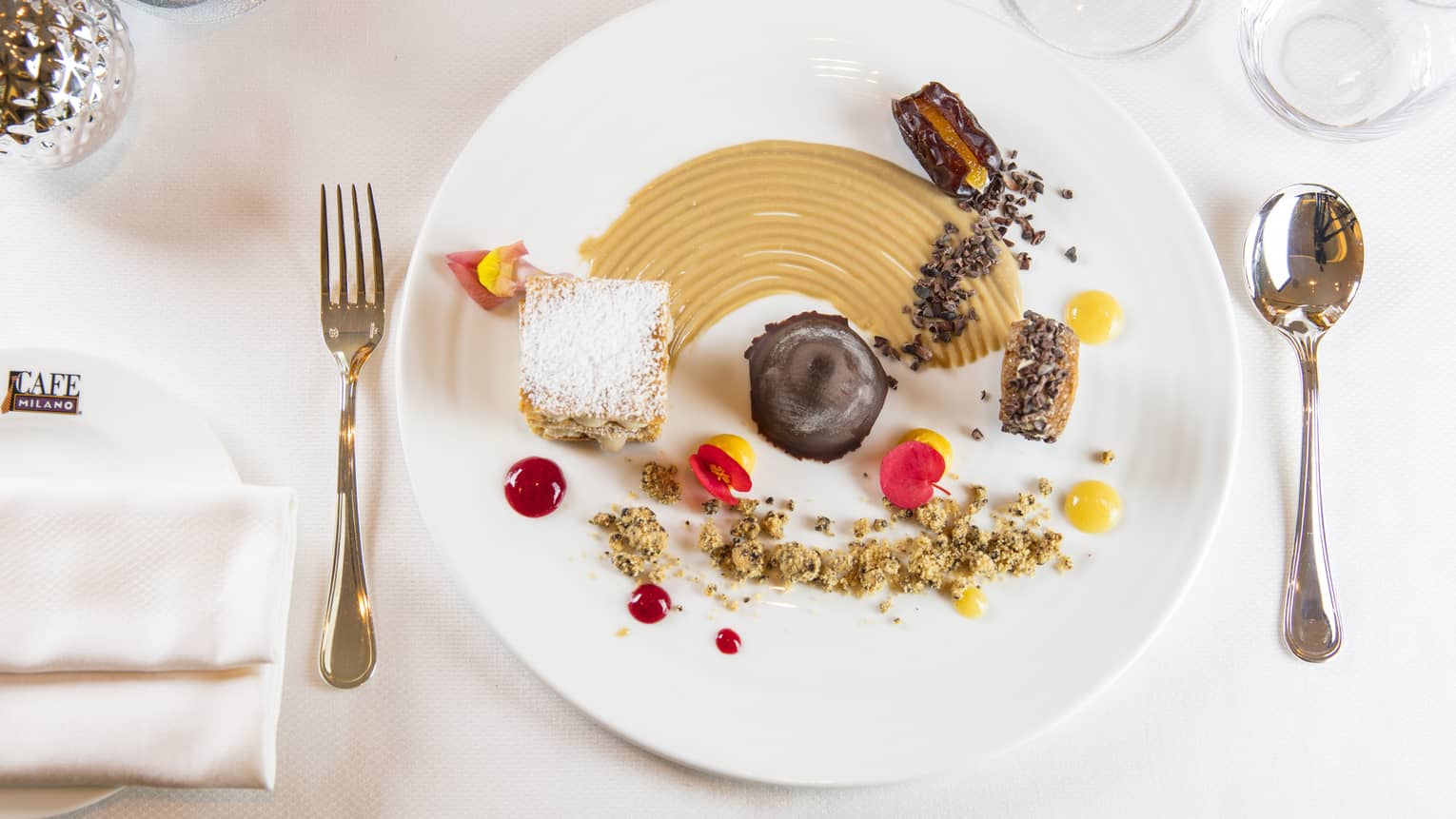 A dessert plate with various decadent mini desserts on it, on a clean white plate and white table cloth