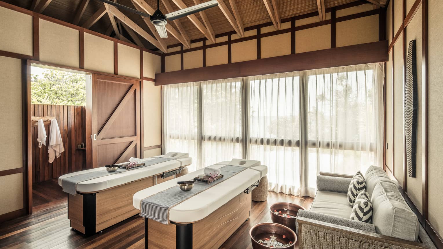 Two massage tables with copper bowls by wicker sofa, spa tubs