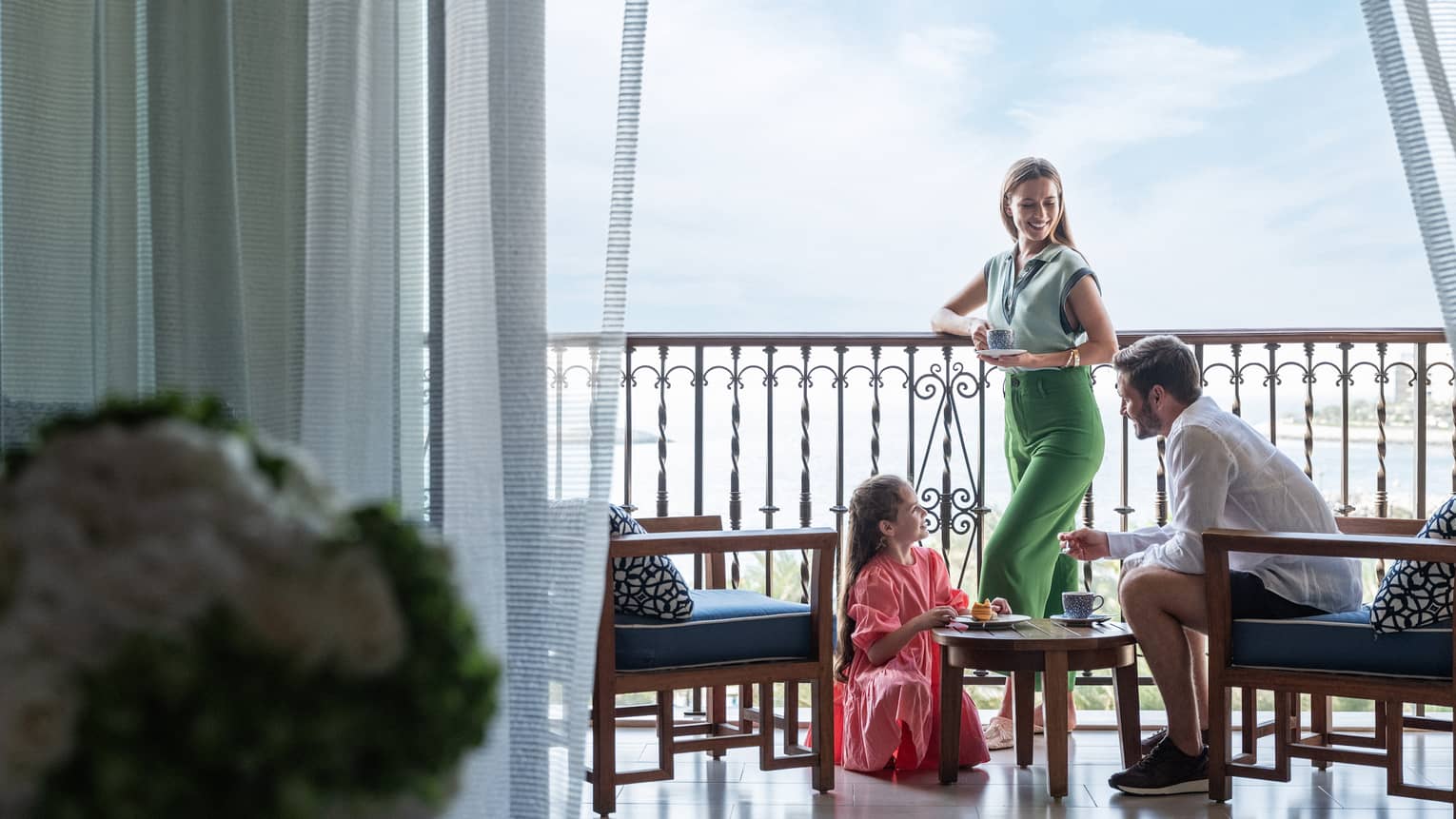 A couple and their daughter stand on a balcony below a bright blue sky.
