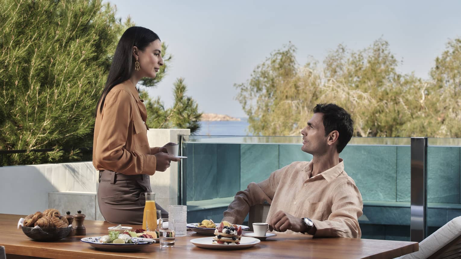 A couple dines together outdoors with a pool and ocean view behind