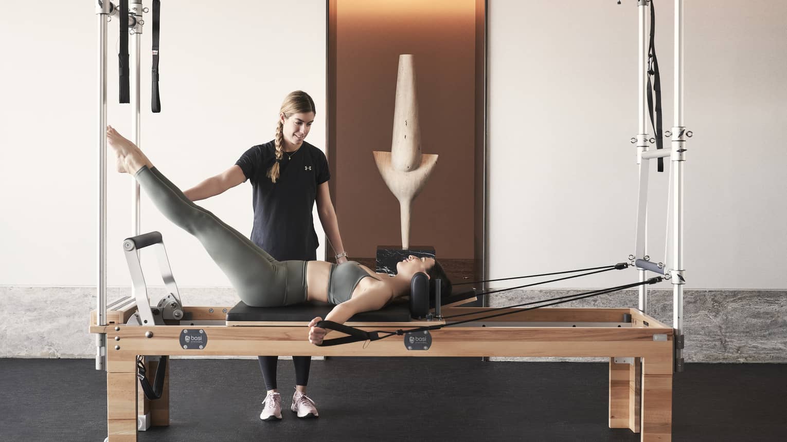 Fitness coach holds legs of woman lying and working out on a Pilates reformer