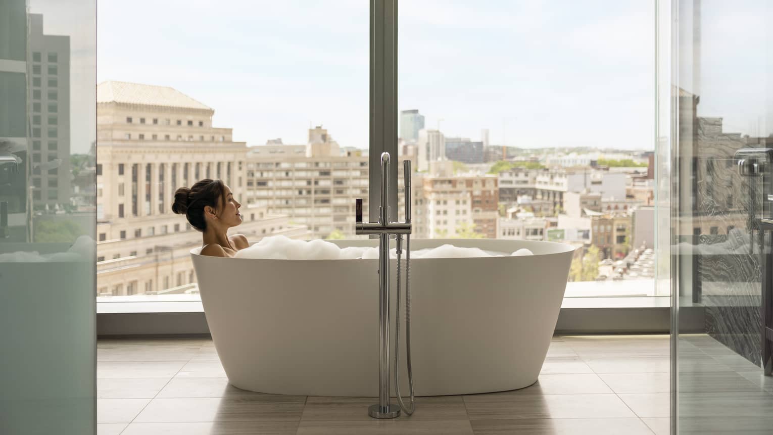 A woman in a bathtub next to a large window.