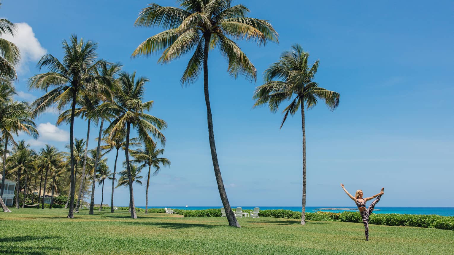 A person doing a yoga pose outside near the ocean and palm trees