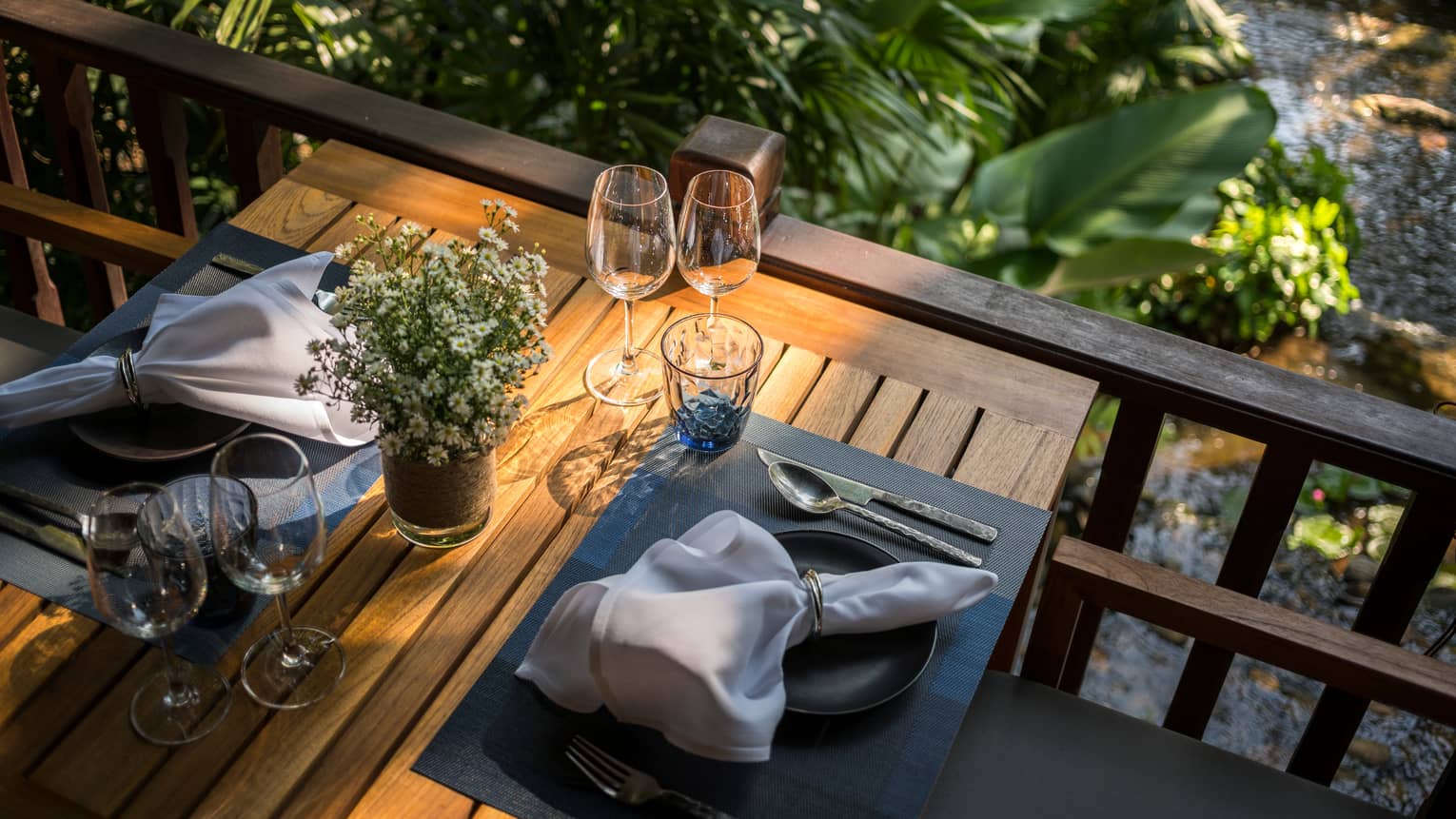 Aerial view of wood patio dining table with two place settings, white napkins, flowers